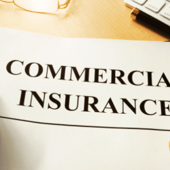 A paper document with the words "COMMERCIAL INSURANCE" in bold text sits on the desk surface, partially obscuring the edge of a keyboard and a pair of eyeglasses. Nearby, information about group retirement plans can be seen peeking out from beneath the document.