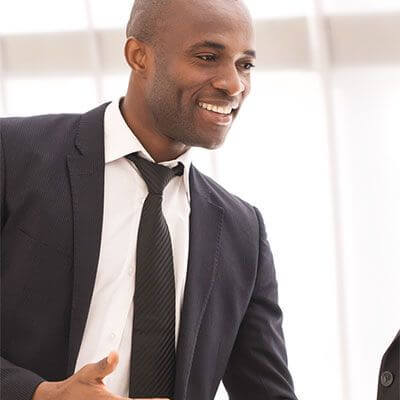 A man in a business suit and tie is smiling and looking to the side in a well-lit, modern room. He appears to be in a conversation or meeting about financial planning for business owners, displaying a positive and engaged demeanor.