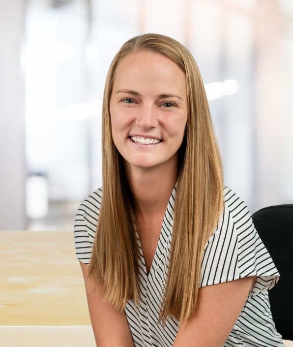 SYM Financial Advisors, an independent, commission-free fiduciary with 55+ years of serving clients: A smiling woman with long blonde hair sits at her desk at SYM Financial Advisors.