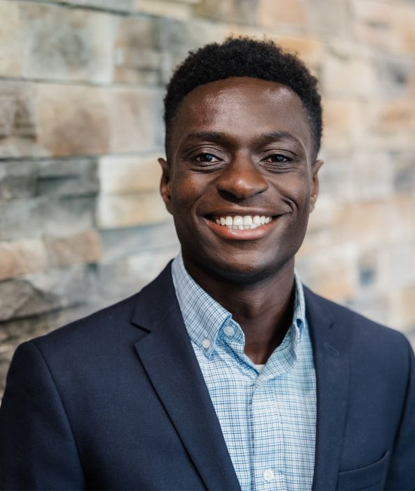 man in a blue suit coat with light blue shirt and dark curly short hair