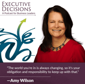 A woman with long dark hair, wearing a red top and a black necklace, smiles at the camera. A quote below reads, “The world you're in is always changing, so it's your obligation and responsibility to keep up with that." —Amy Wilson. Text on top reads "Executive Decisions: A Podcast for Business Leaders.
