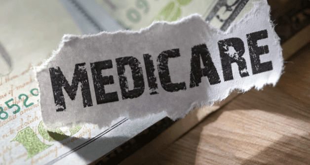 A close-up image of the word "Medicare" printed on a torn piece of paper positioned over a background that includes U.S. currency. It signifies financial aspects related to Medicare health insurance.