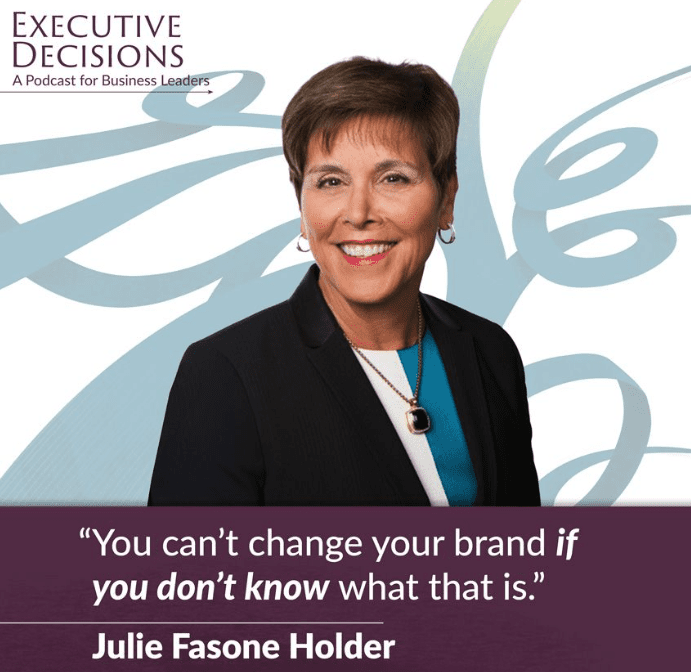 A woman with short brown hair, wearing a dark blazer over a blue top and a necklace, smiles at the camera. The background features a light abstract design. Text on the image reads: "Executive Decisions: A Podcast for Business Leaders" and "Julie Fasone Holder: 'You can't change your brand if you don’t know what that is.'" This podcast offers insights from influential corporate women.