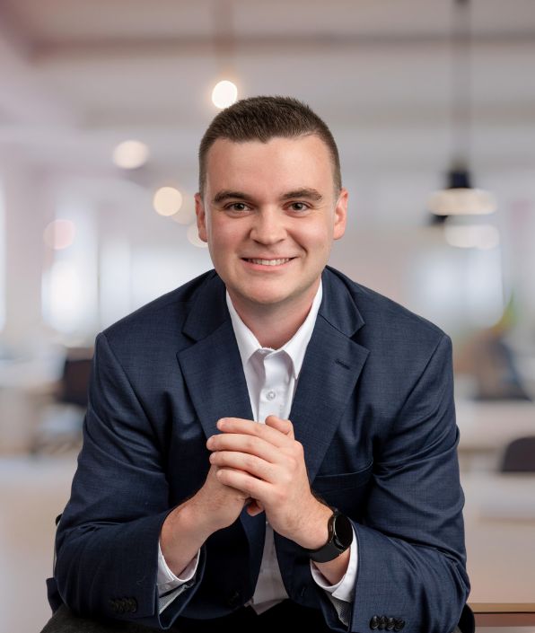 SYM Financial Advisors, an independent, commission-free fiduciary with 55+ years of serving clients: A SYM Financial Advisors fiduciary in a navy suit and white shirt smiling with his hands clasped.