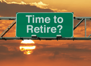 A green road sign reads "Time to Retire?" with a picturesque sunset and clouds in the background. The sun is partially visible, creating a warm and serene atmosphere, inviting thoughts of exiting corporate life for something more tranquil.