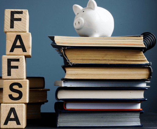 A piggy bank sits atop a stack of books on the right, while wooden blocks on the left spell out "FAFSA" vertically. The background is neutral, contrasting with the books and blocks, hinting at upcoming FAFSA changes.
