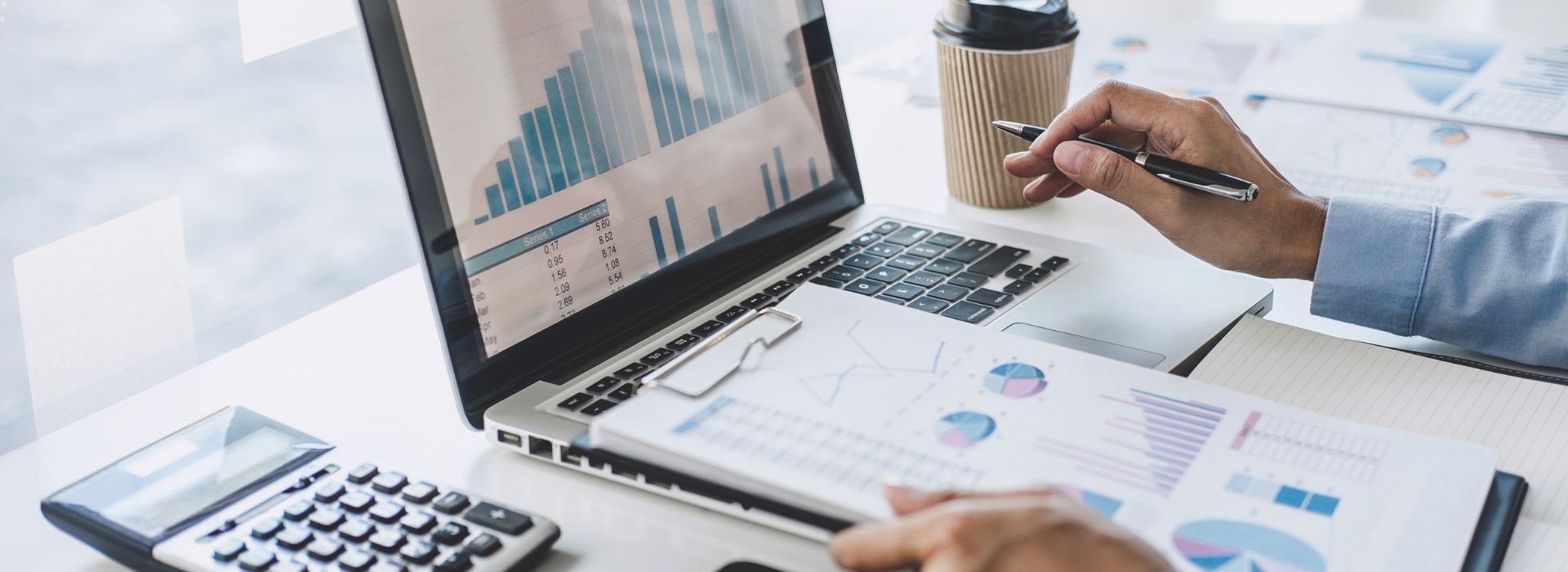 a desk full of papers with charts and graphs and a computer and a coffee cup