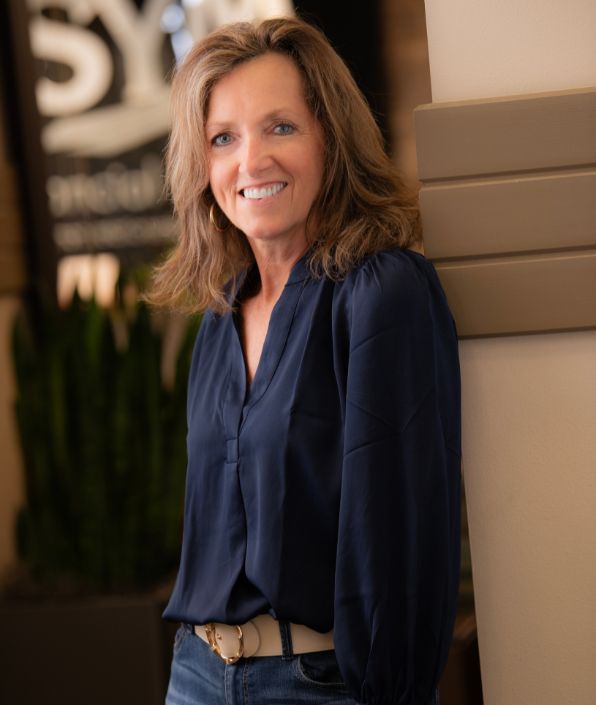 woman wearing a navy blue blouse leaning against a wall with SYM written in the background
