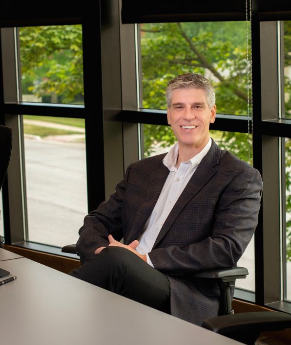 gray haired man in suit coat sitting casually at a conference table