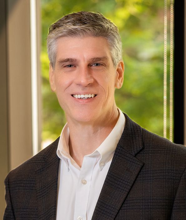 gray haired man in suit coat in front of a window
