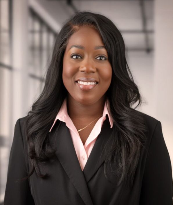 A woman with dark long hair and dark skin in a black blazer with pink collared shirt underneath.