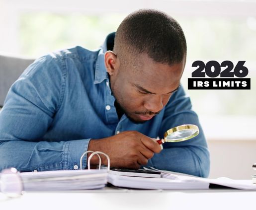 A dark skinned man is looking over a binder of IRS rules with a magnifying glass