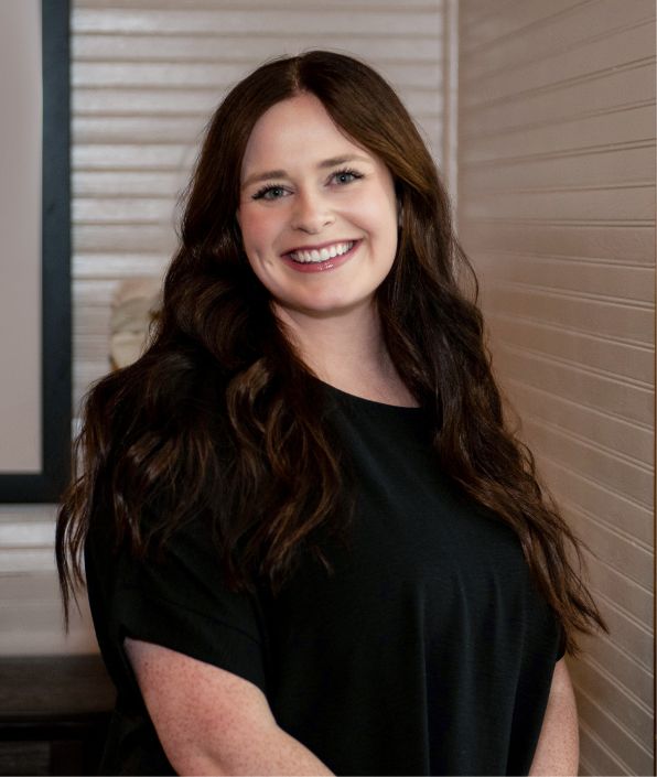 a young woman with long brown hair in a black shirt standing by a white wall