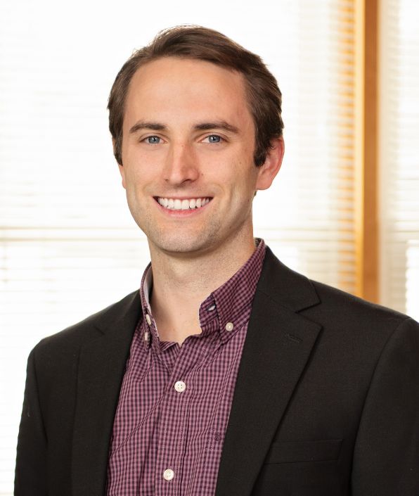 young man with brown hair in a black suit coat with a burgundy patterned button down shirt