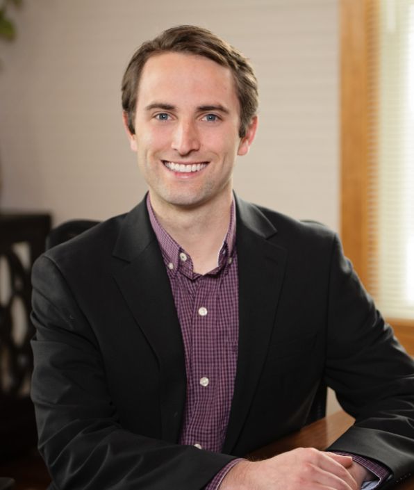 young man with brown hair in a black suit coat with a burgundy patterned button down shirt