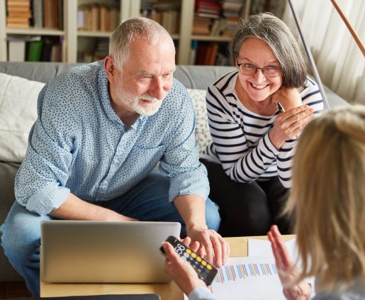 a middle aged couple talking across a couch table with an advisor who has a calculator