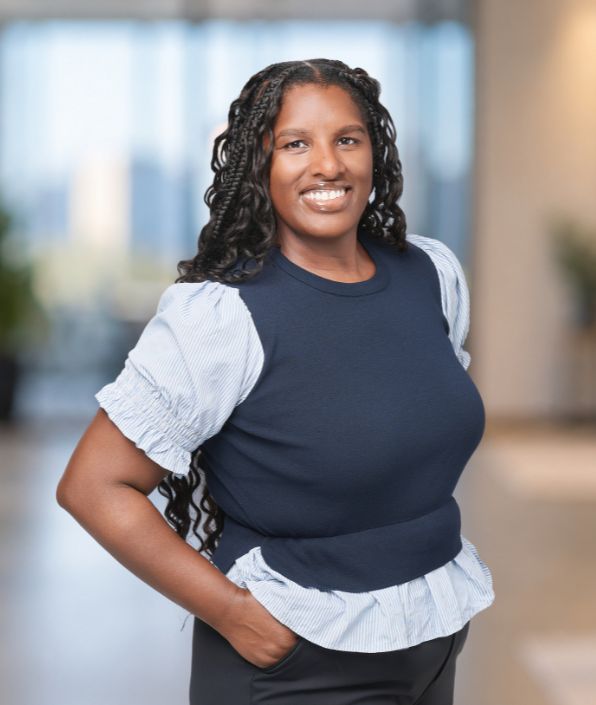 woman with long dark curly hair in a white blouse with a navy blue sweater vest