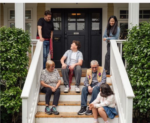 A multi-generational family sits together on the front porch steps of a family cabin, reflecting the multi-generational planning supported by SYM Financial Advisors, an independent, commission-free fiduciary with 55+ years of serving clients.