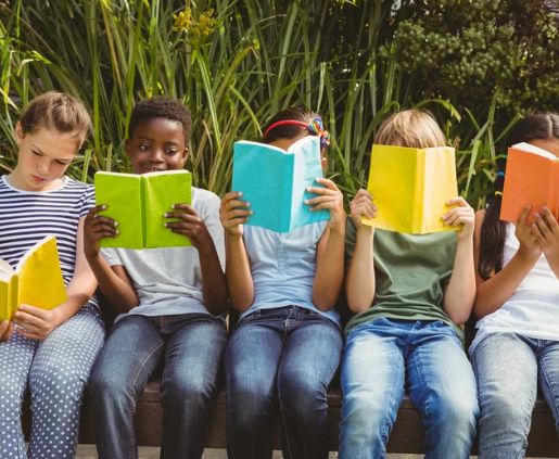 Five children sit on a bench, each holding an open book about 529 plan rules in front of their face, reflecting the educational focus of SYM Financial Advisors, an independent, commission-free fiduciary with 55+ years of serving clients.
